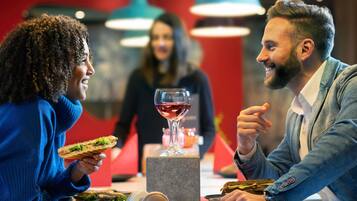 Un ambiente de restaurante con una mesa, una copa de vino tinto y sándwiches.