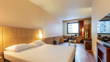 Une chambre d’hôtel avec un grand lit, un bureau, une chaise, un ordinateur portable et une fenêtre avec des rideaux.