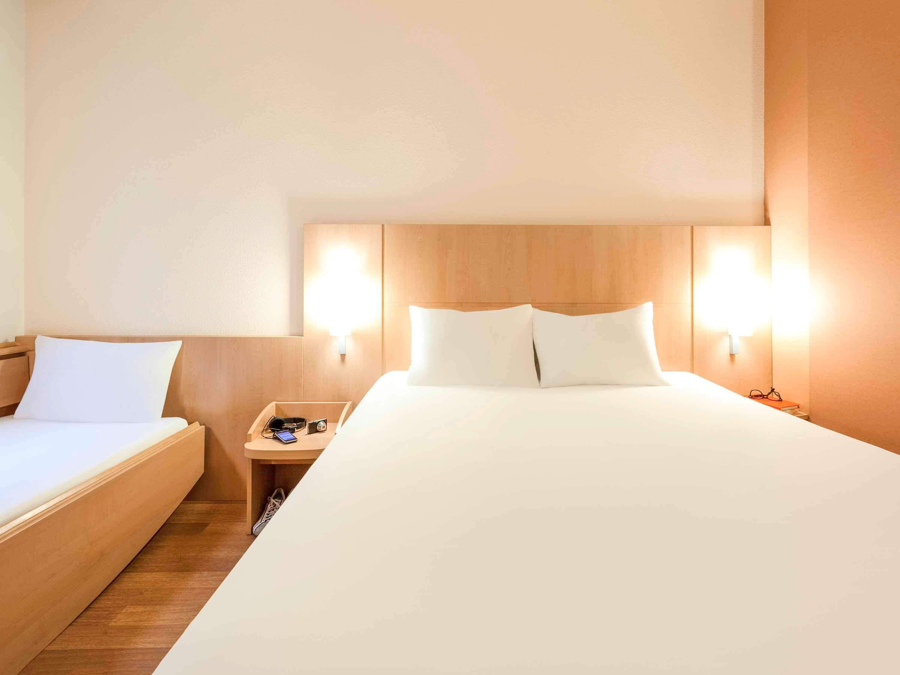 Habitació d'hotel amb un llit gran, un llit més petit, dues taules de nit i làmpades penjades a la paret.