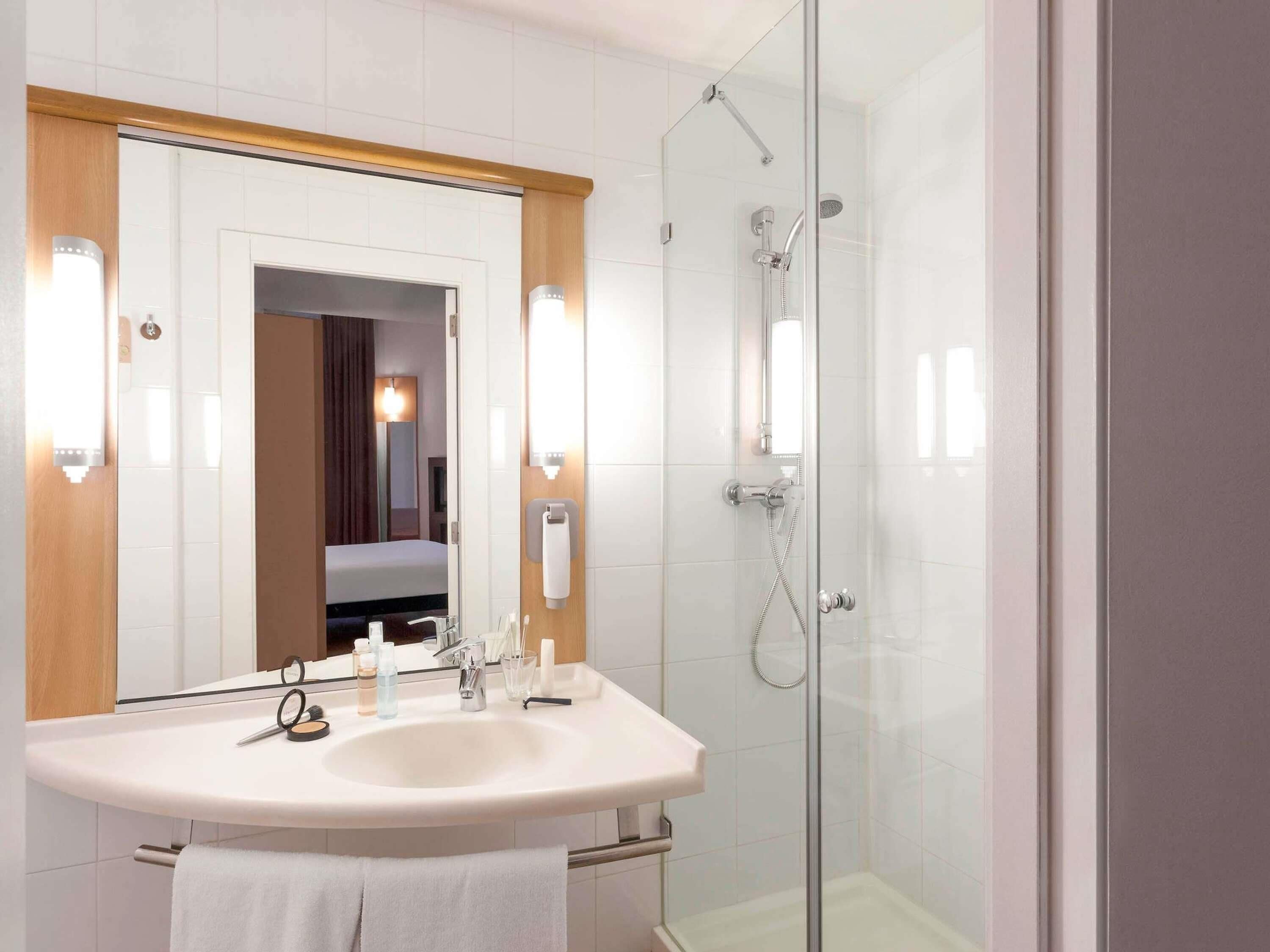 Une salle de bain moderne avec un grand miroir, un lavabo, une douche et un porte-serviettes.