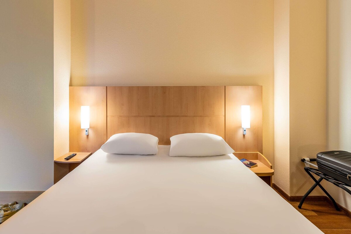 A hotel room with a large bed, two bedside tables, and a wooden headboard.