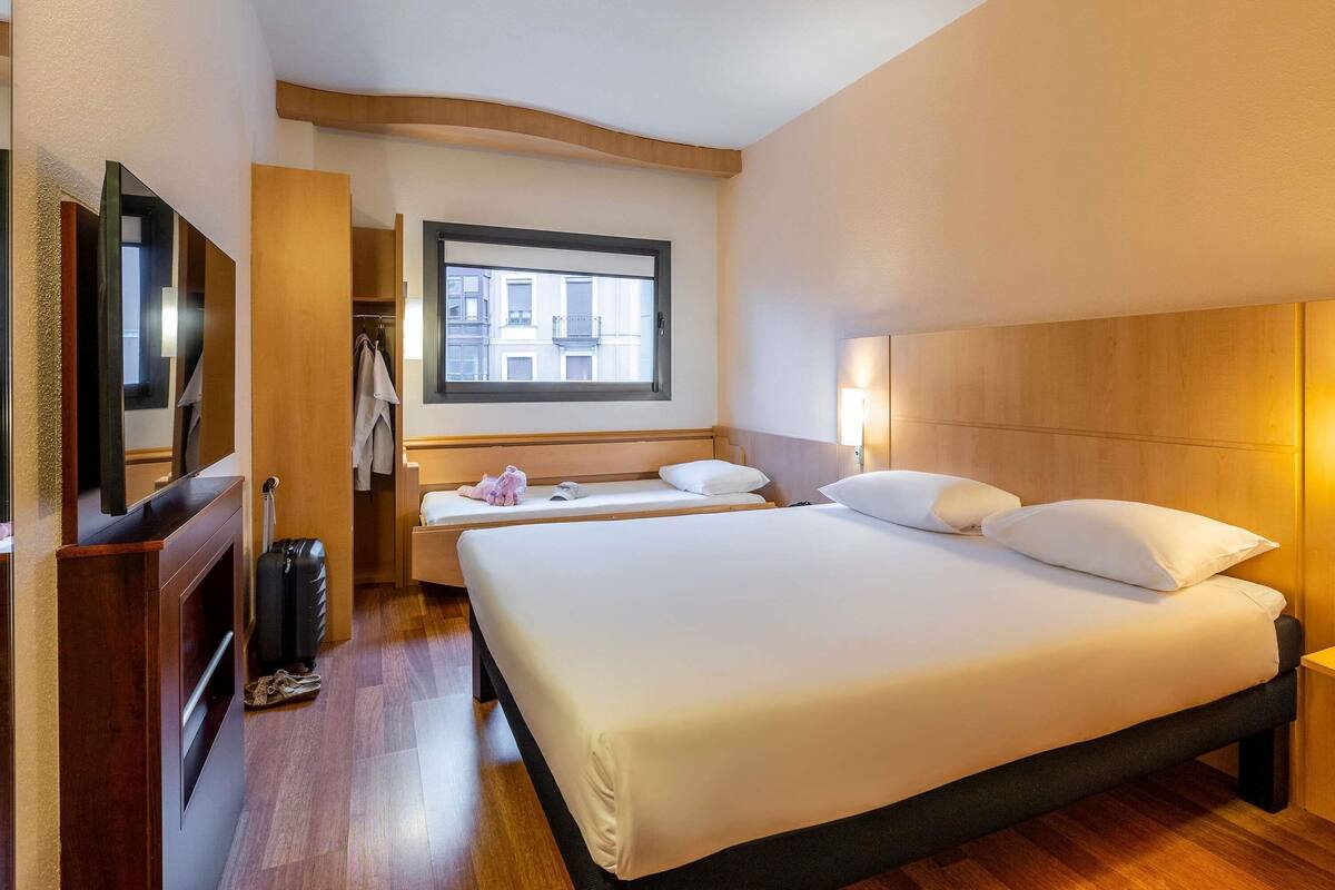 A hotel room with a large bed, a TV, a wardrobe, and a window with a city view.