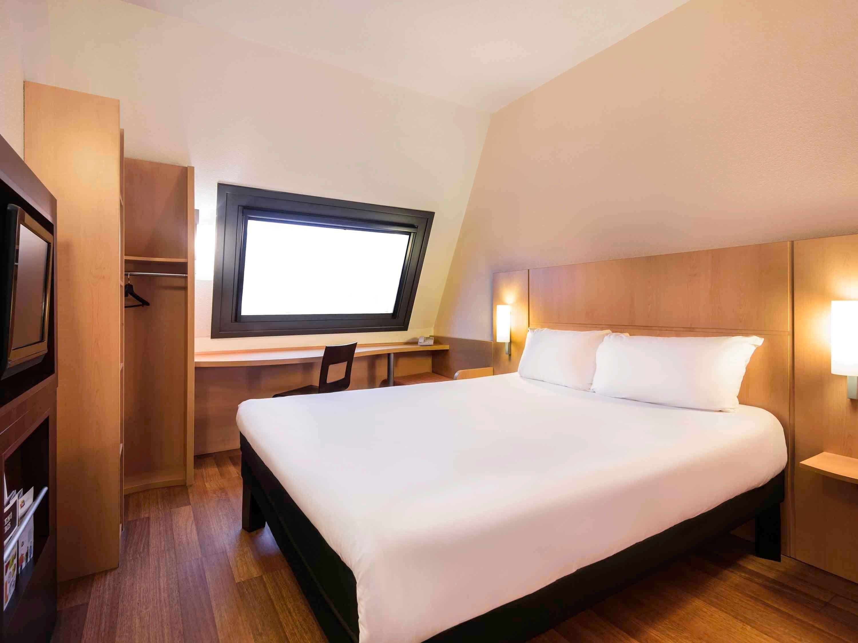 Une chambre d’hôtel avec un lit, un bureau, une télévision et une armoire.