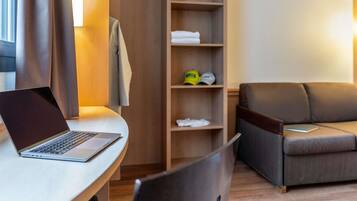 Una habitación de hotel moderna con una laptop sobre un escritorio, un sofá y un armario de madera con estantes.