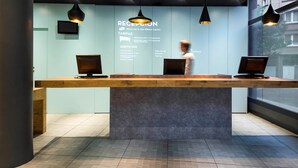 Un mostrador de recepción con dos computadoras, un cartel informativo y luminarias colgantes.