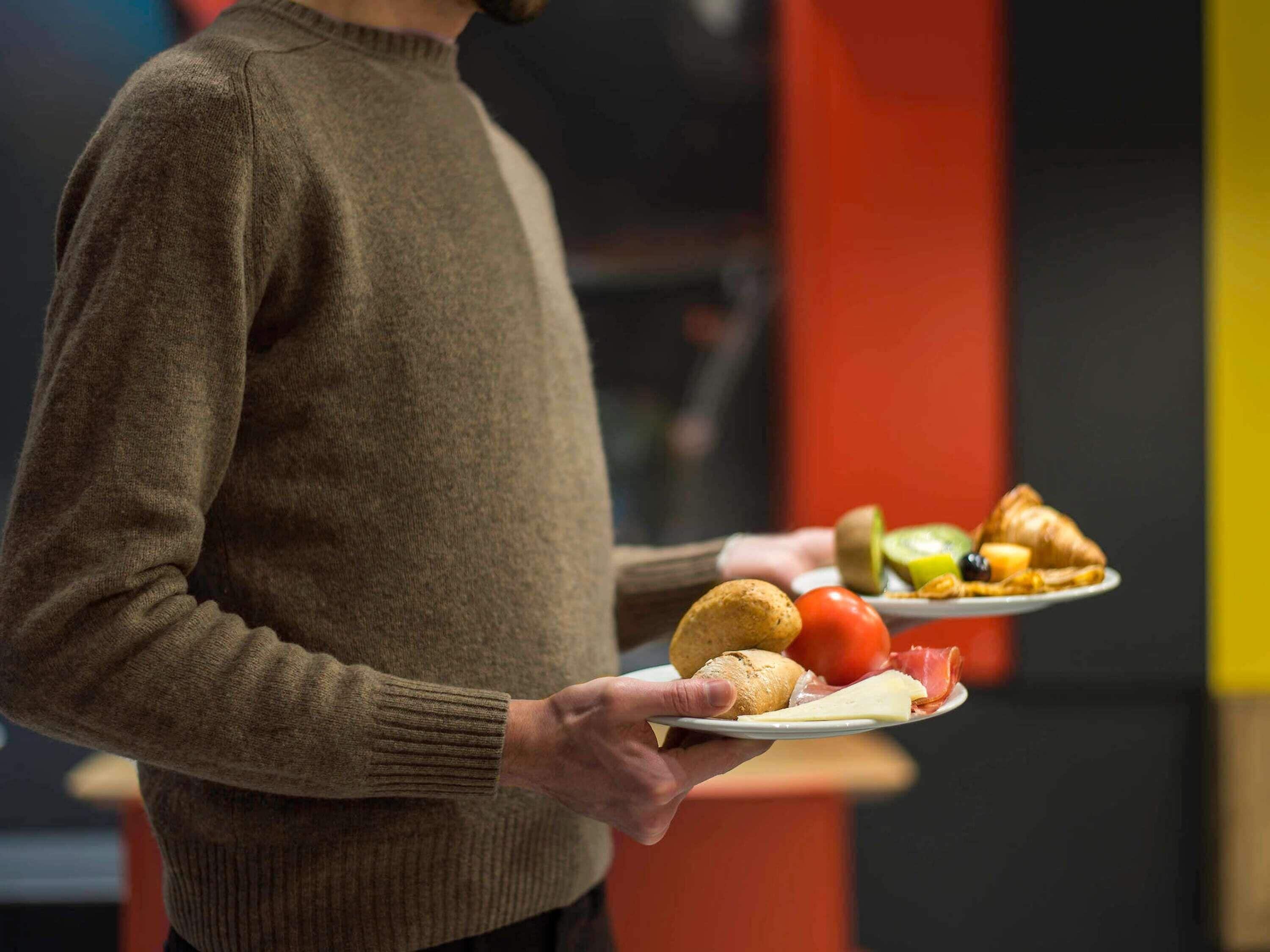 Una persona sosteniendo un plato con comida que incluye pan, queso y verduras.