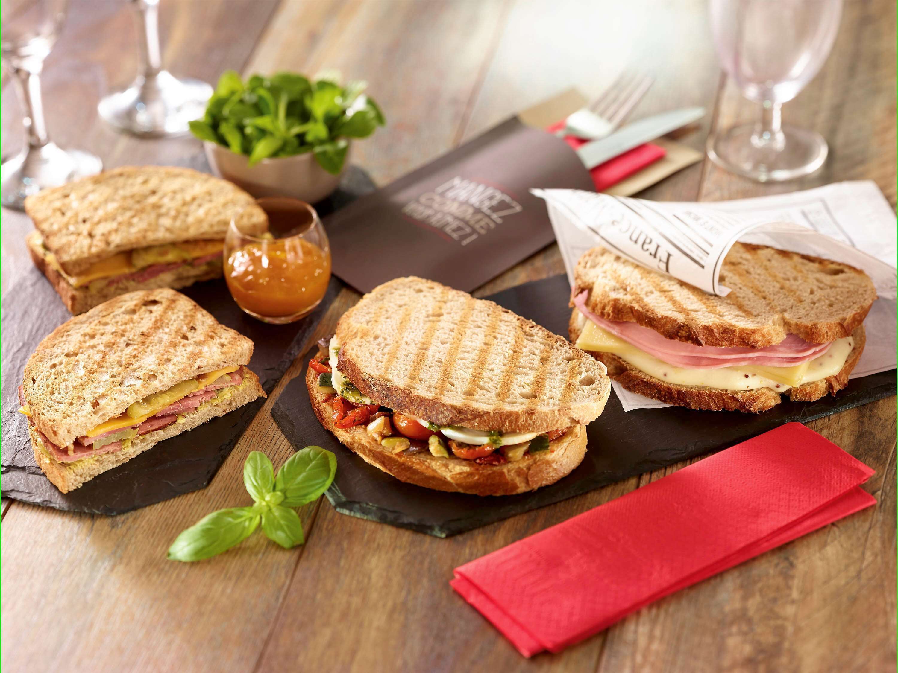 A sandwich with ham, cheese, and vegetables on a wooden table.