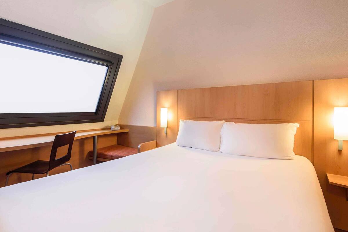 A hotel room with a large bed, a desk, a chair, and a window.