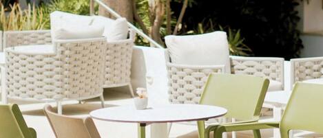 Mobiliario exterior con sillas blancas y verdes, una mesa blanca y una palmera de fondo.