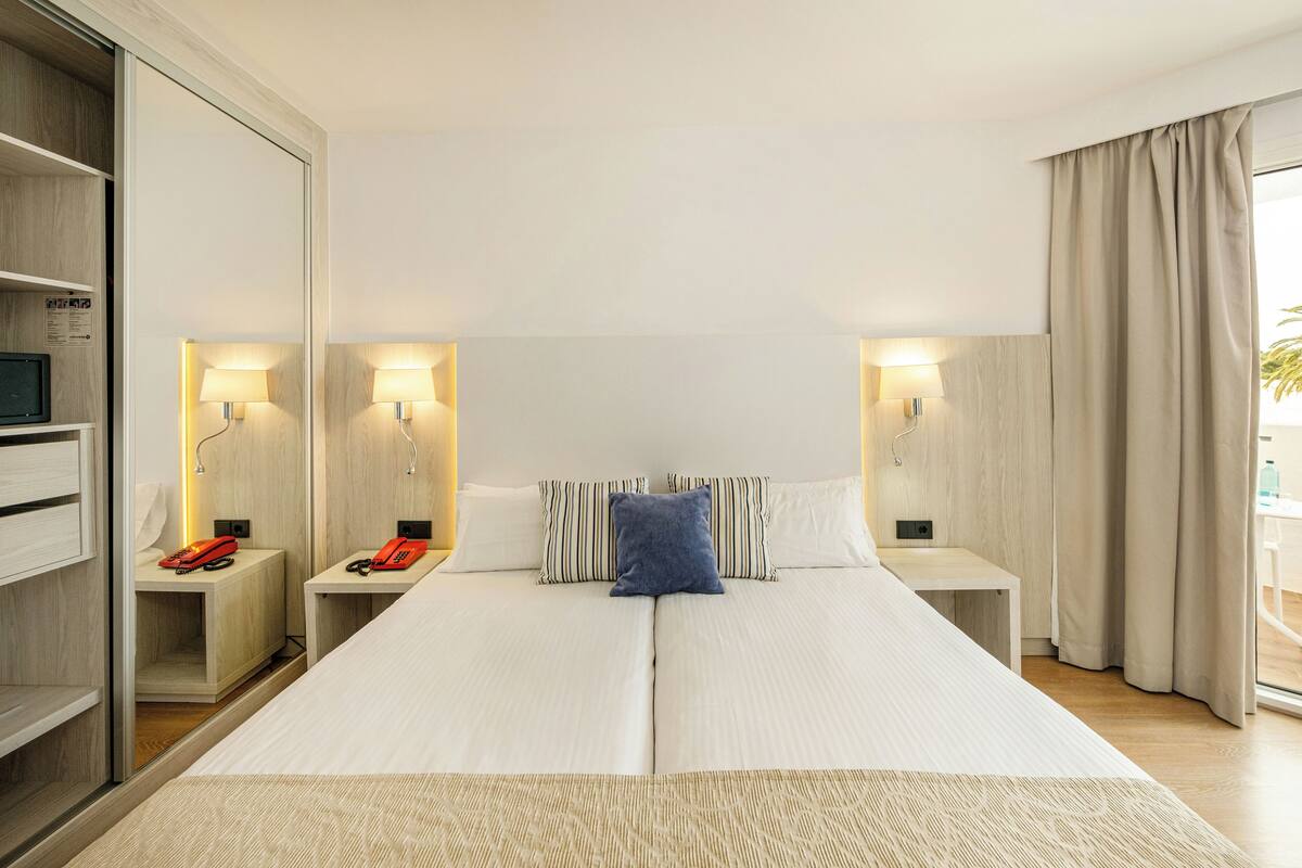 A hotel room with a large bed, bedside tables with lamps, a wardrobe, and a view of the outdoors.