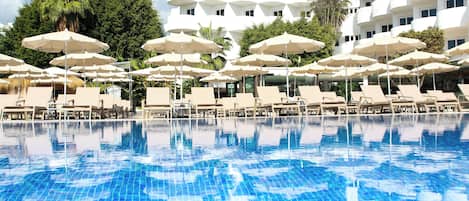 A swimming pool with lounge chairs and umbrellas, surrounded by a white building with multiple balconies.