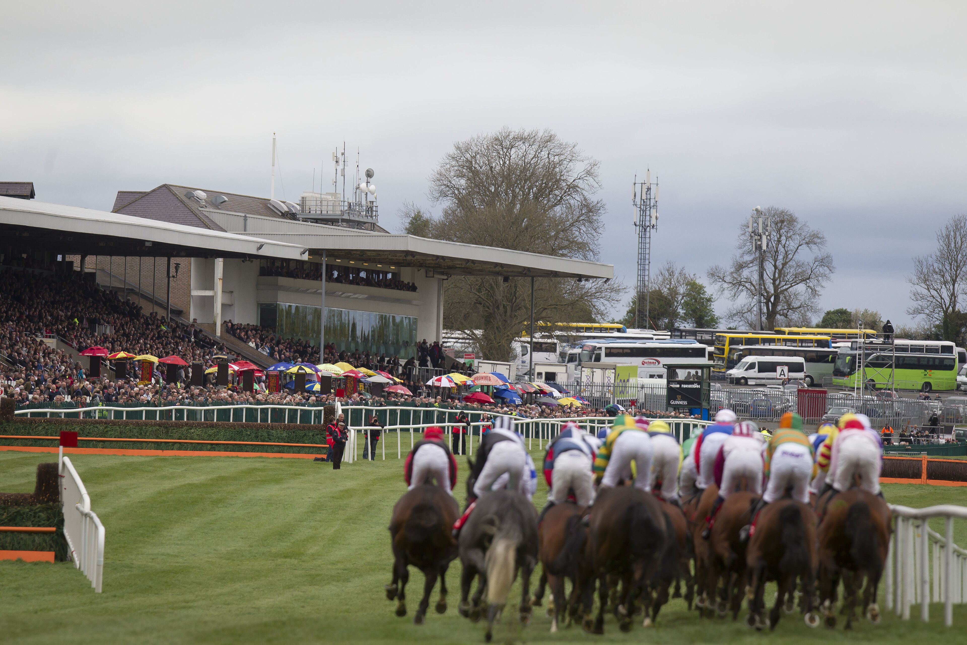 Una carrera de caballos con jinetes, una multitud de espectadores y un edificio grande al fondo.