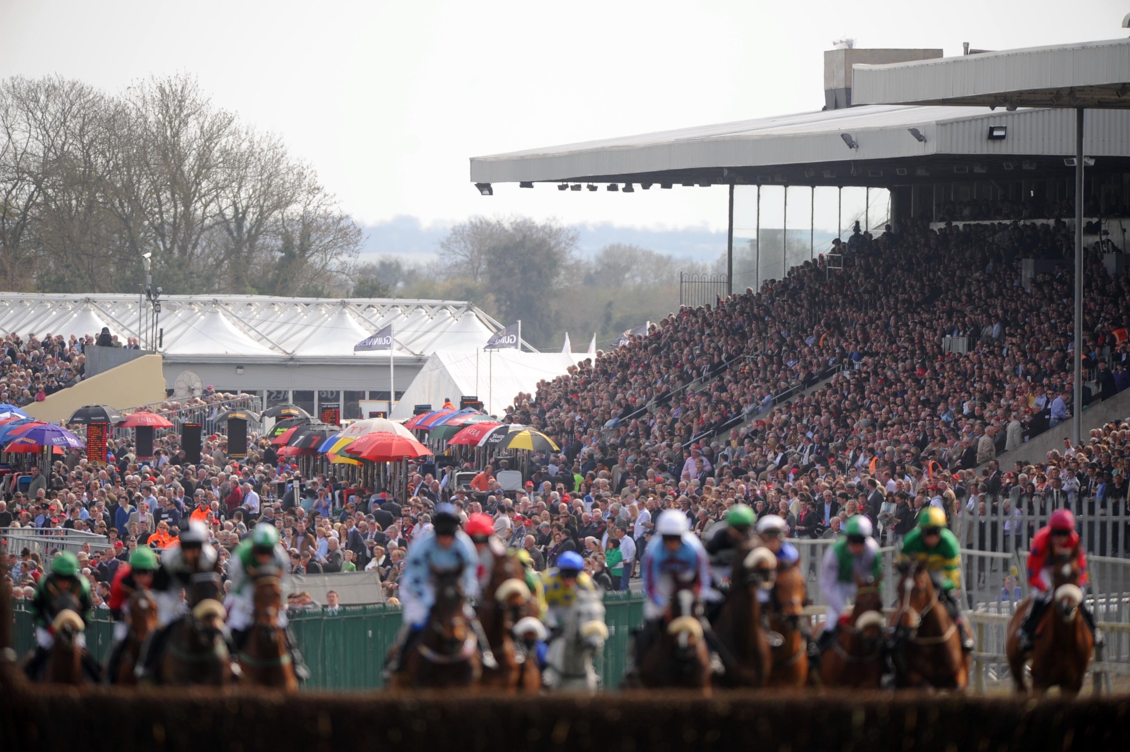 A crowded outdoor event with people on horseback, spectators in the stands, and tents.