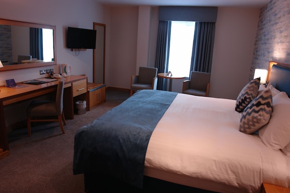 A hotel room with a bed, desk, chairs, a television, and a window with curtains. - Westgrove Hotel (Clane)