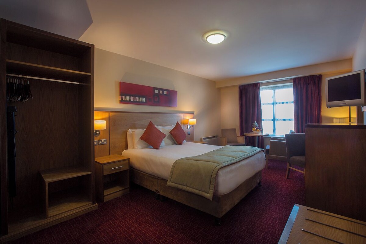 Habitación de hotel con una cama grande, un armario, un escritorio, una silla y un televisor.