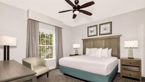 A hotel room with a bed, a chair, a desk, a nightstand, a ceiling fan, and two framed pictures on the wall. - Club Wyndham at the Cottages (North Myrtle Beach)