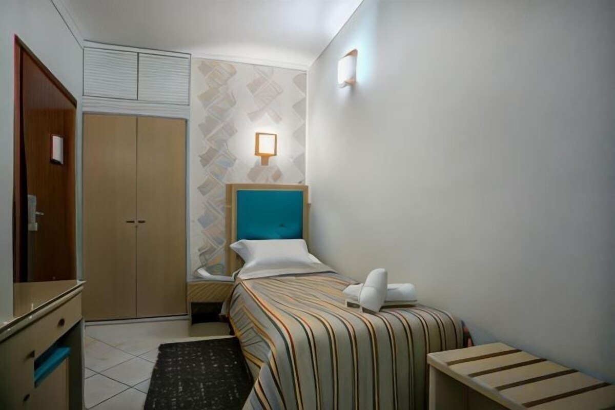 A hotel room with a bed, a bedside table, a wardrobe, and a wall-mounted light fixture.