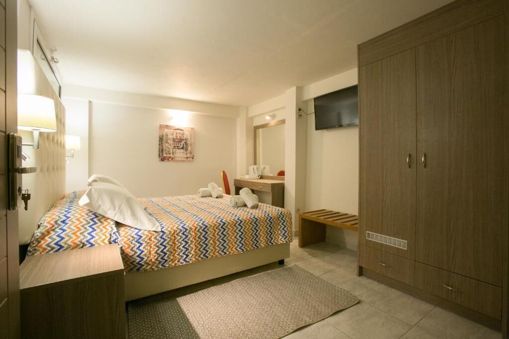 A hotel room with a bed, a desk, a wardrobe, a television, and a wall-mounted artwork.