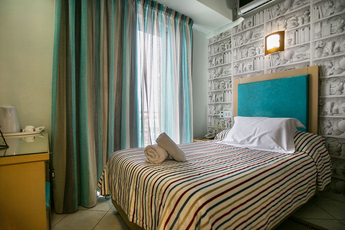 Une chambre d’hôtel avec un lit, des rideaux, une table de chevet, une lampe et un mur orné de motifs en relief.