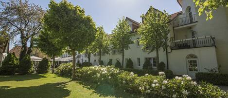 A building with a white facade, a balcony with a black railing, and a garden with white flowers.