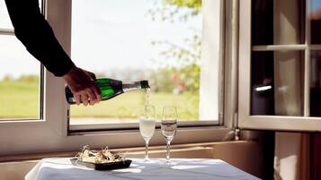 A bottle being poured into two glasses on a table by a window.