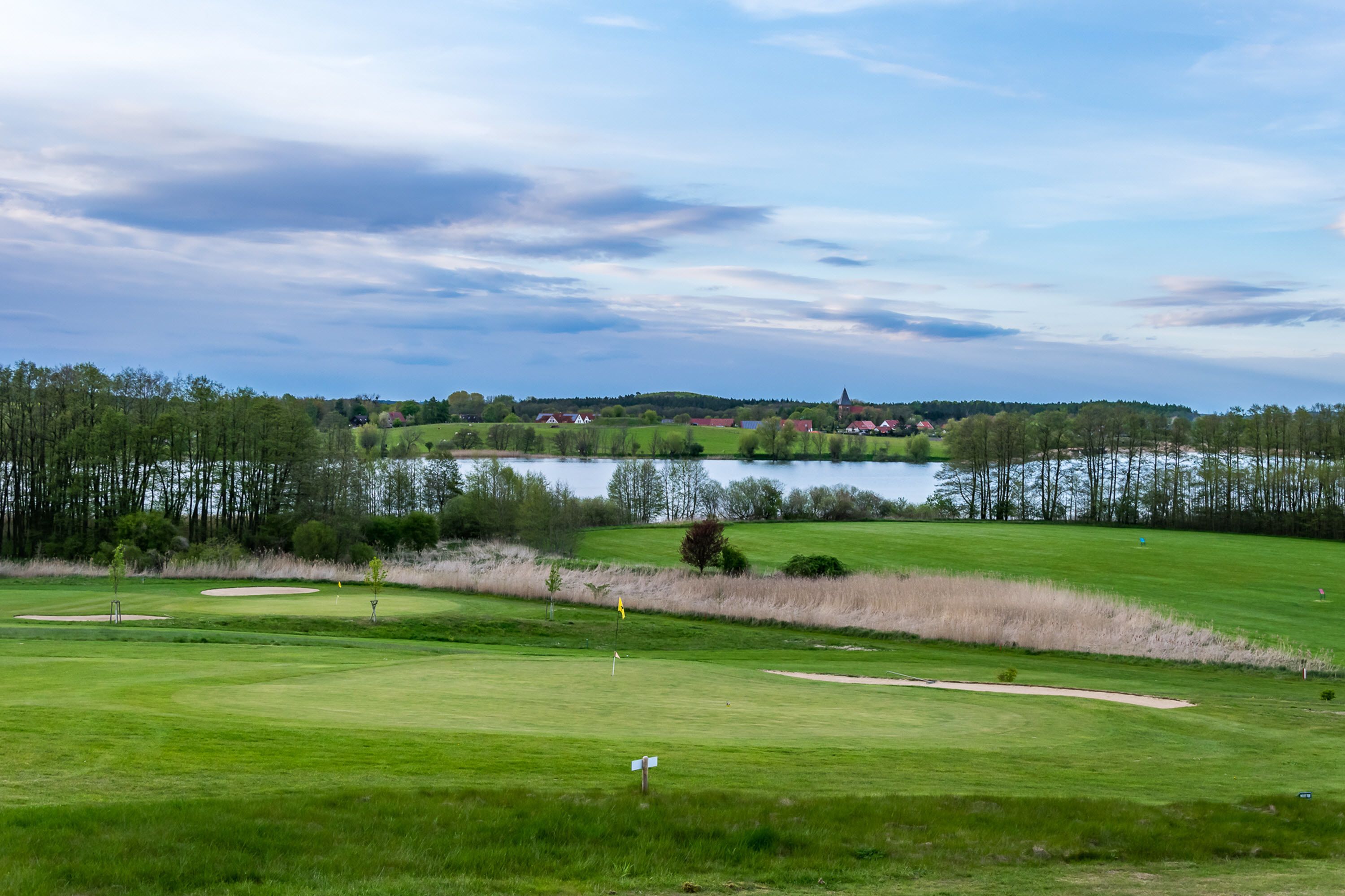 Un campo da golf con un lago, alberi e una cittadina in lontananza.