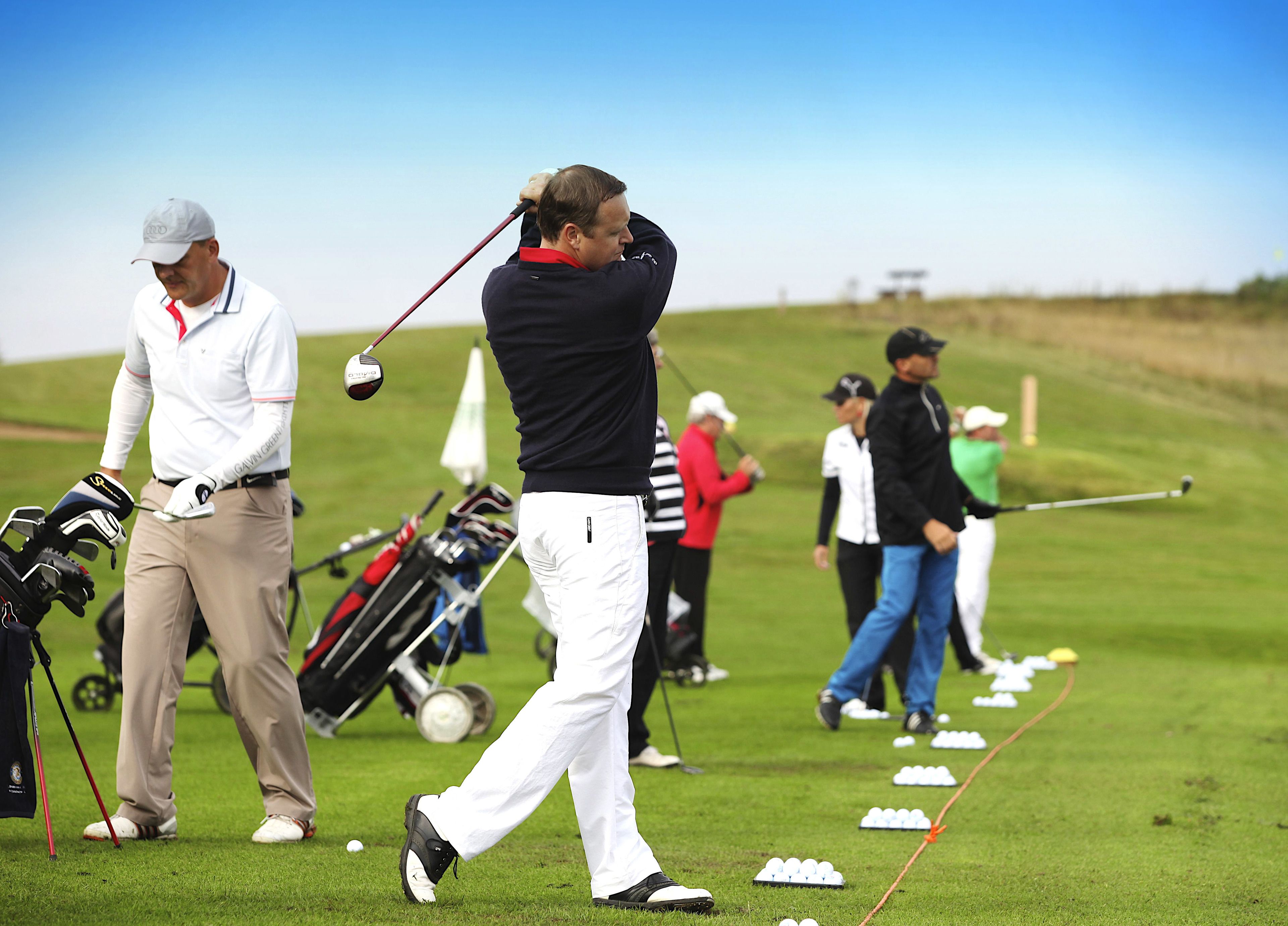 Un campo de golf con jugadores en movimiento, bolsas de golf y palos.