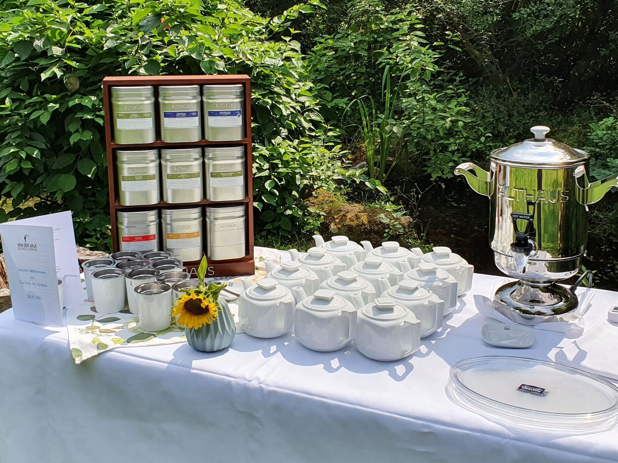 A table with tea dispensers, a sign, and a hot water dispenser in an outdoor setting.