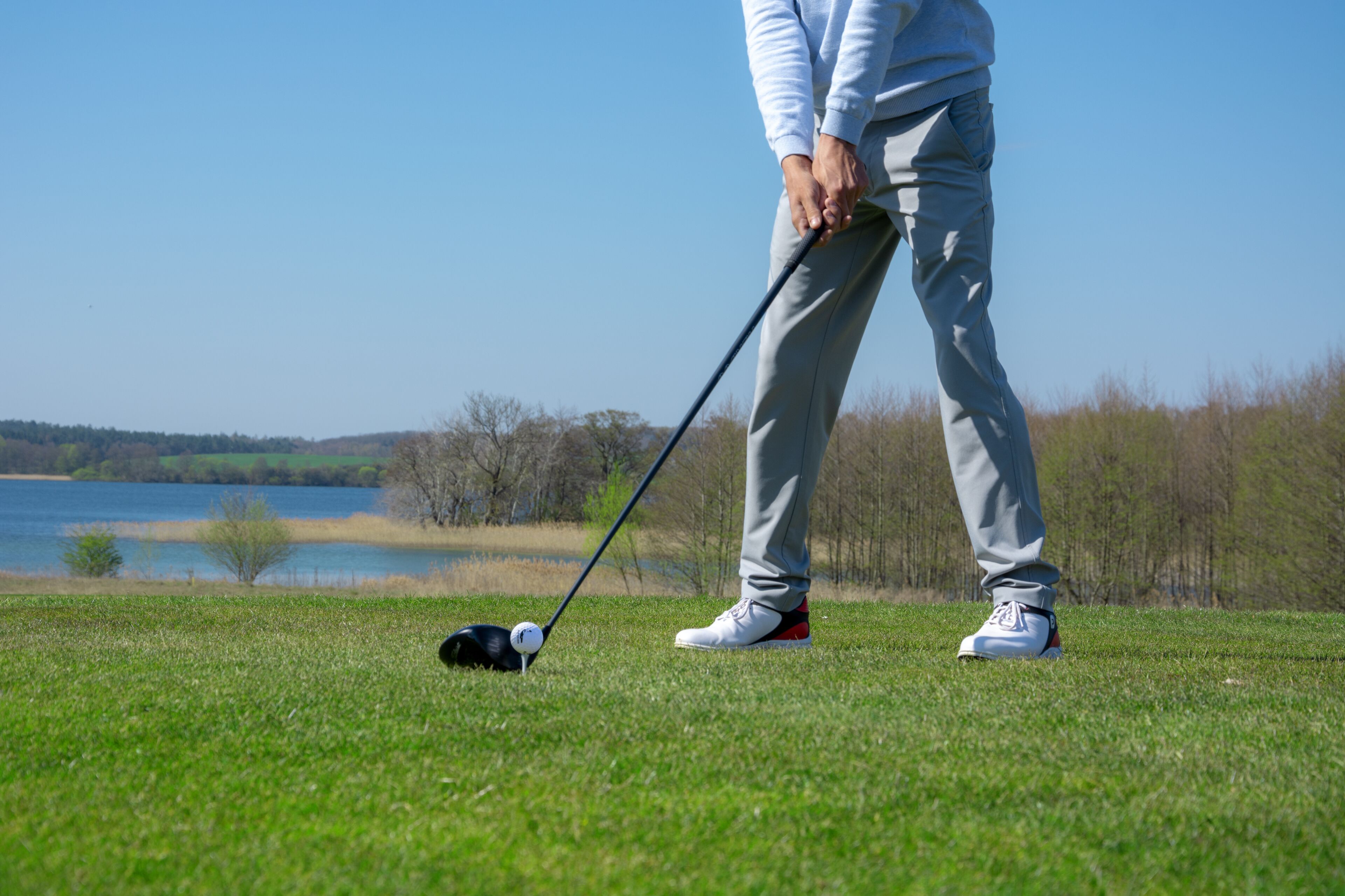 A person on a golf course with a golf club, a golf ball, and a clear view of a lake and trees in the background.