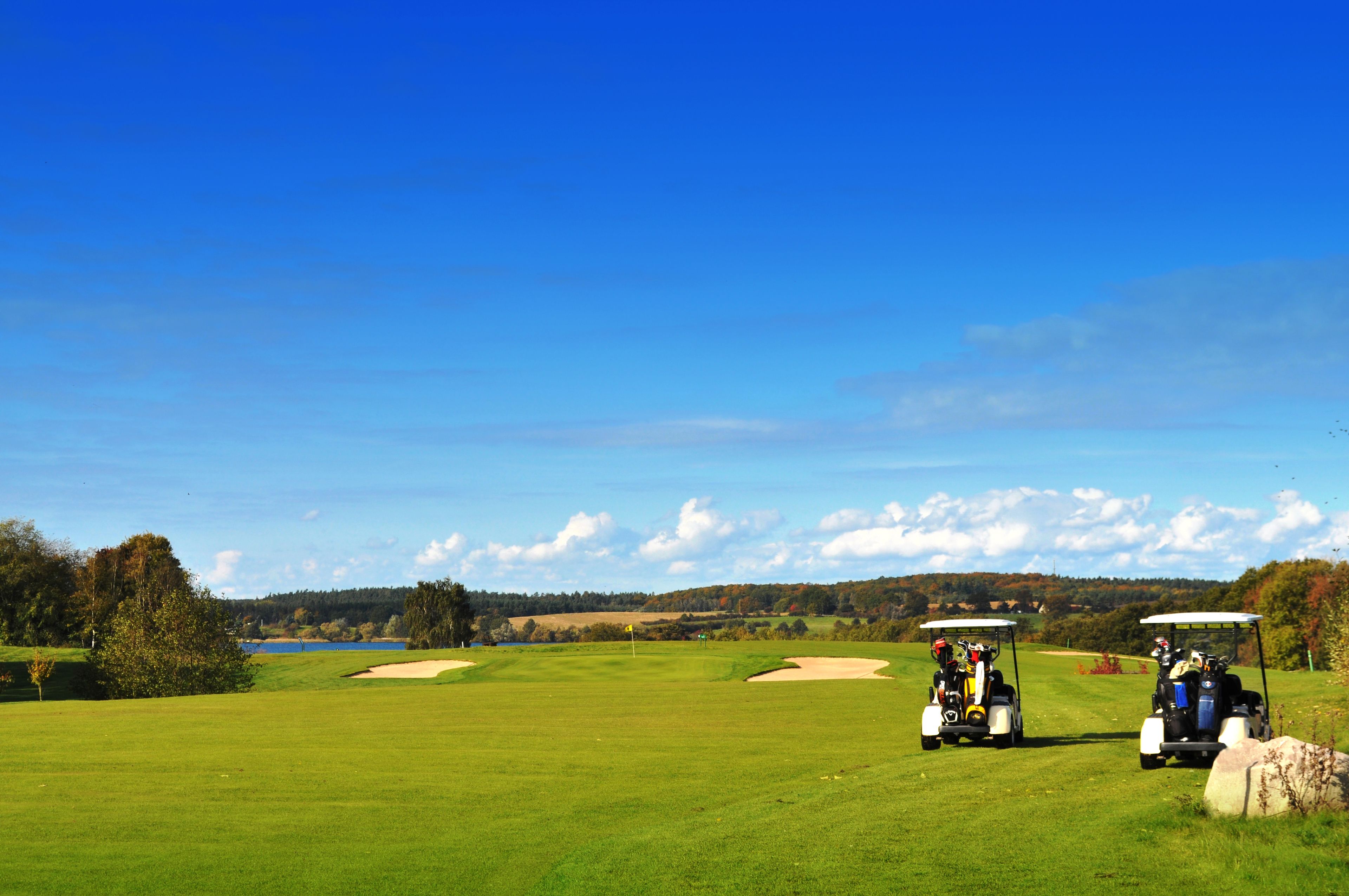 Een golfbaan met twee golfkarren en een heldere blauwe lucht.