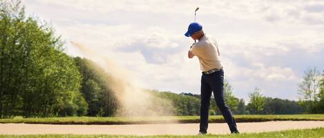 A person playing golf on a course with trees and a clear sky.