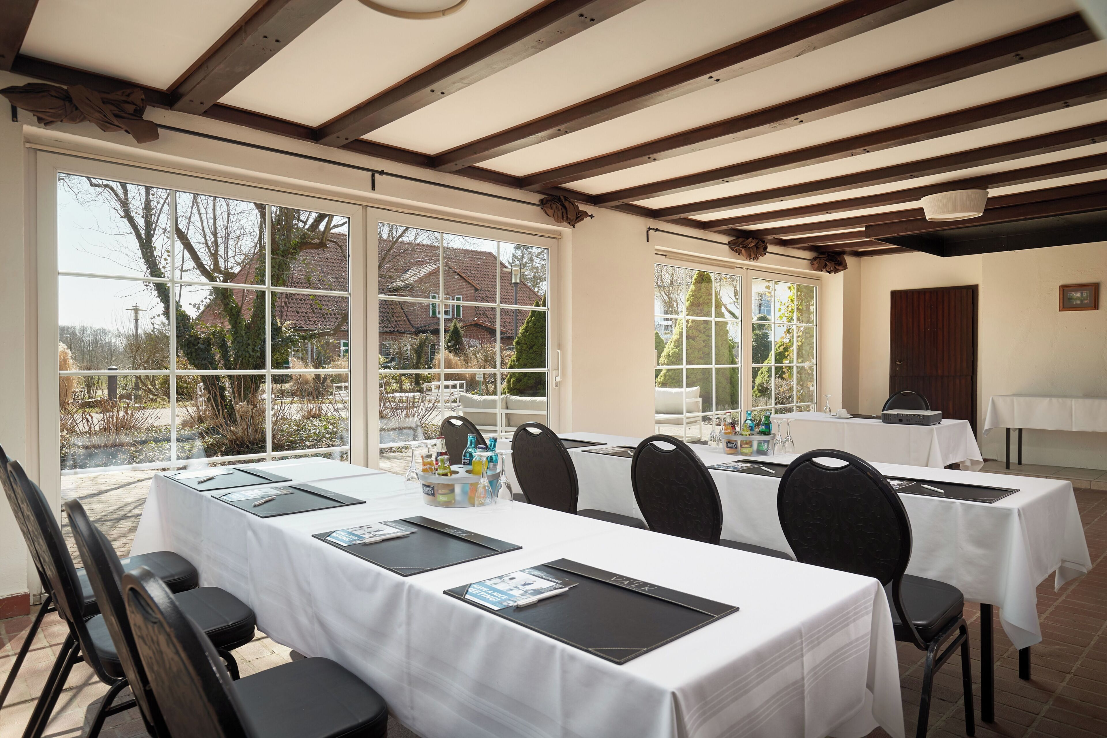 Un salón de conferencias con mesas dispuestas para una reunión, amplias ventanas con vistas al exterior y una estructura de techo de madera.