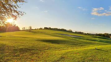 A golf course with a flagstick, rolling hills, and a clear sky.