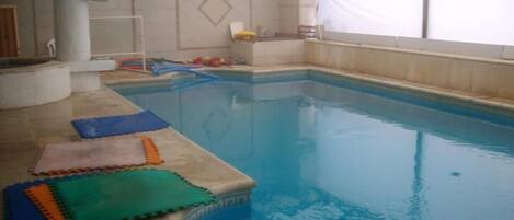 Una piscina interior con suelo de baldosas y zona de borde con esterillas.