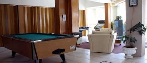 A pool table in a room with wooden paneling, a sofa, and a potted plant.