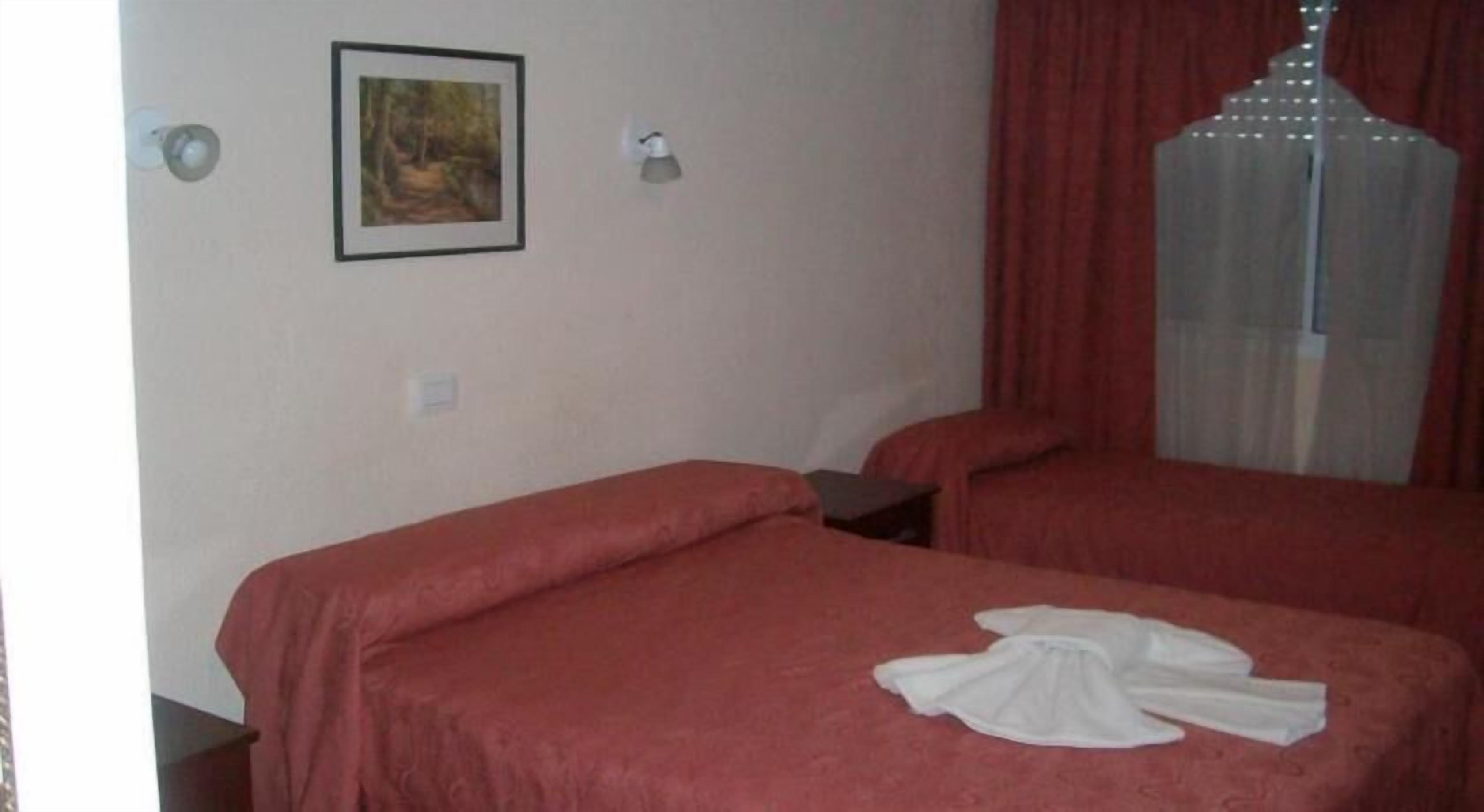Una habitación con dos camas, un cuadro en la pared y una ventana con cortinas.