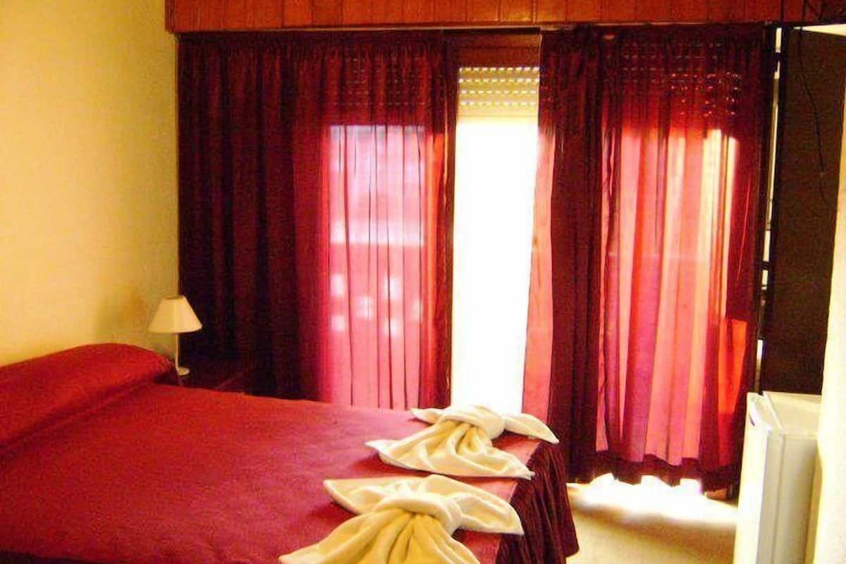 Een hotelkamer met een groot bed, rode gordijnen en een lamp.