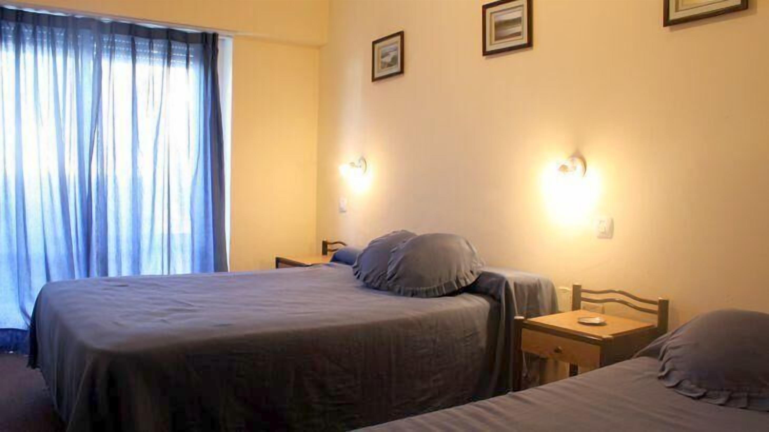 A hotel room with a bed, a bedside table, and a window with curtains.