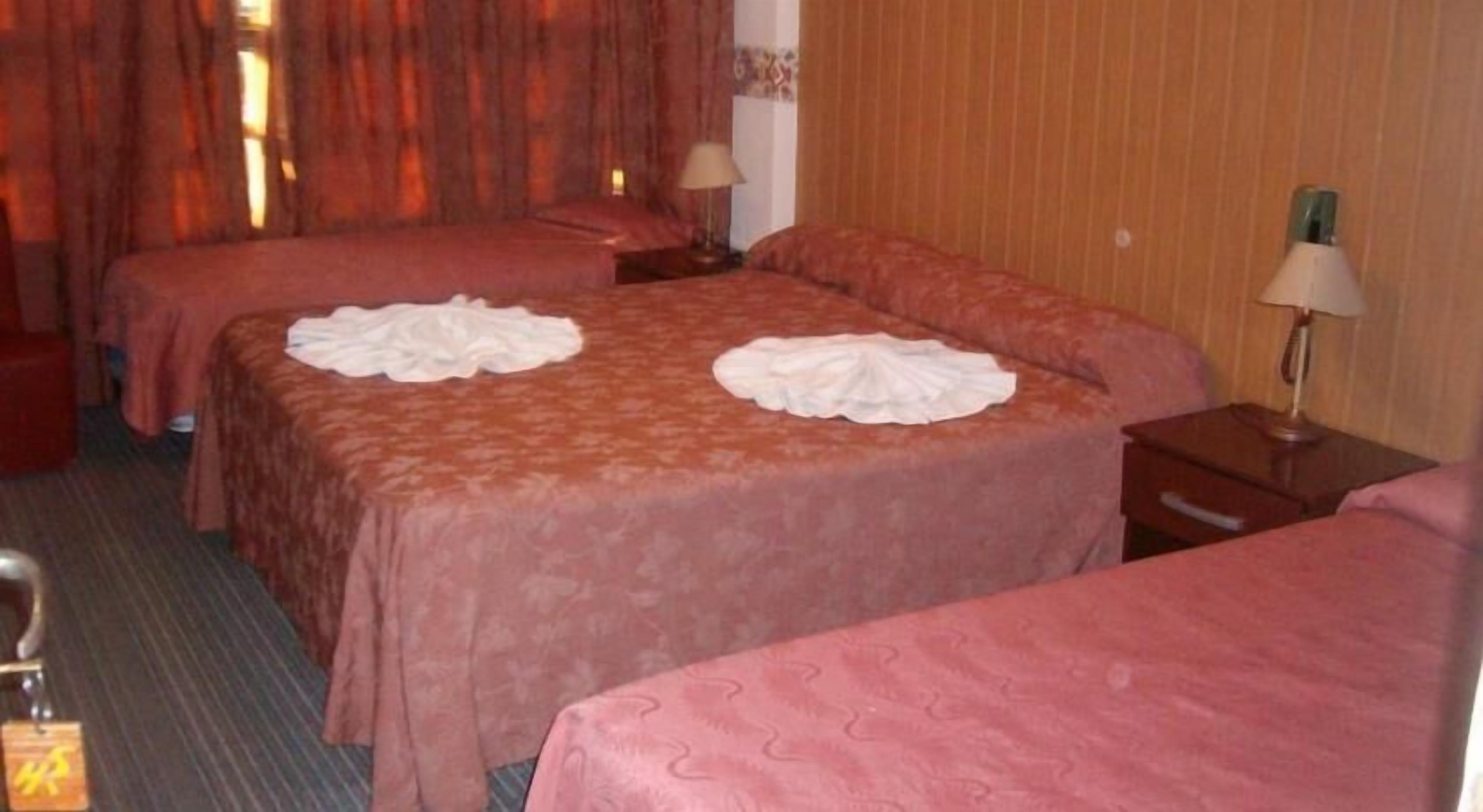 Habitación de hotel con dos camas, cada una con un adorno blanco sobre el edredón.