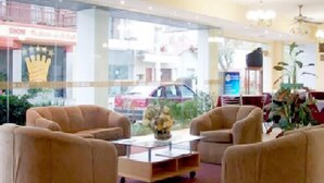 A hotel lobby with beige sofas, a coffee table, and large windows offering a view of the street outside. - San Remo Resort Hotel (Santa Teresita)