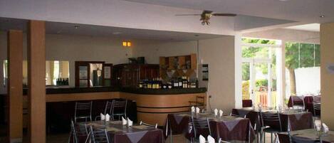 Un restaurante con mesas, sillas, una zona de bar y un ventilador de techo.