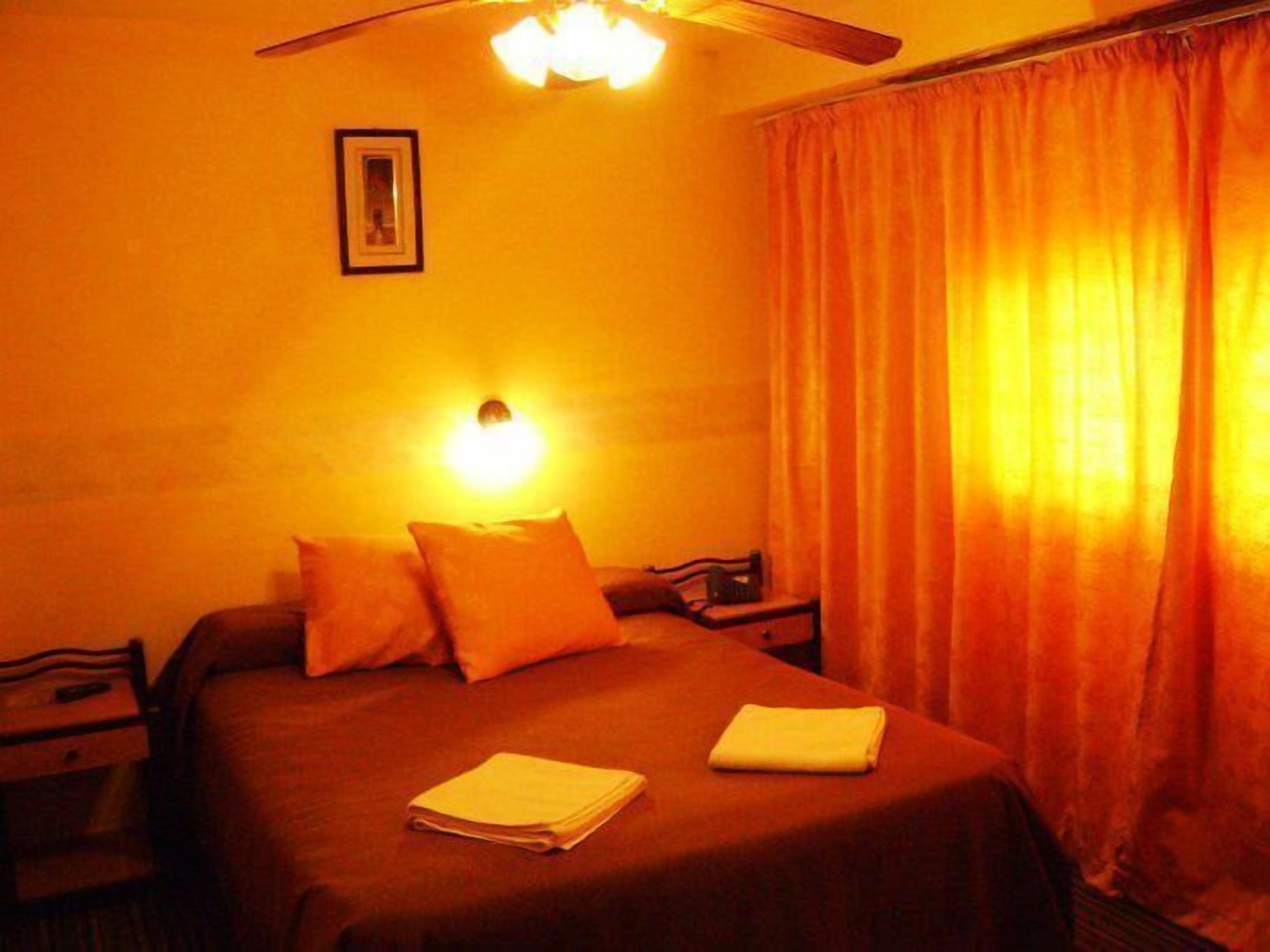 Ein Hotelzimmer mit Bett, Nachttisch, Lampe und einem Fenster mit Vorhängen.