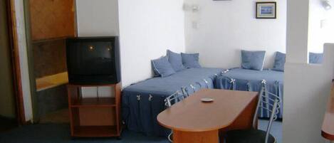 A small, compact room with a single bed, a television, a small table, and a chair.