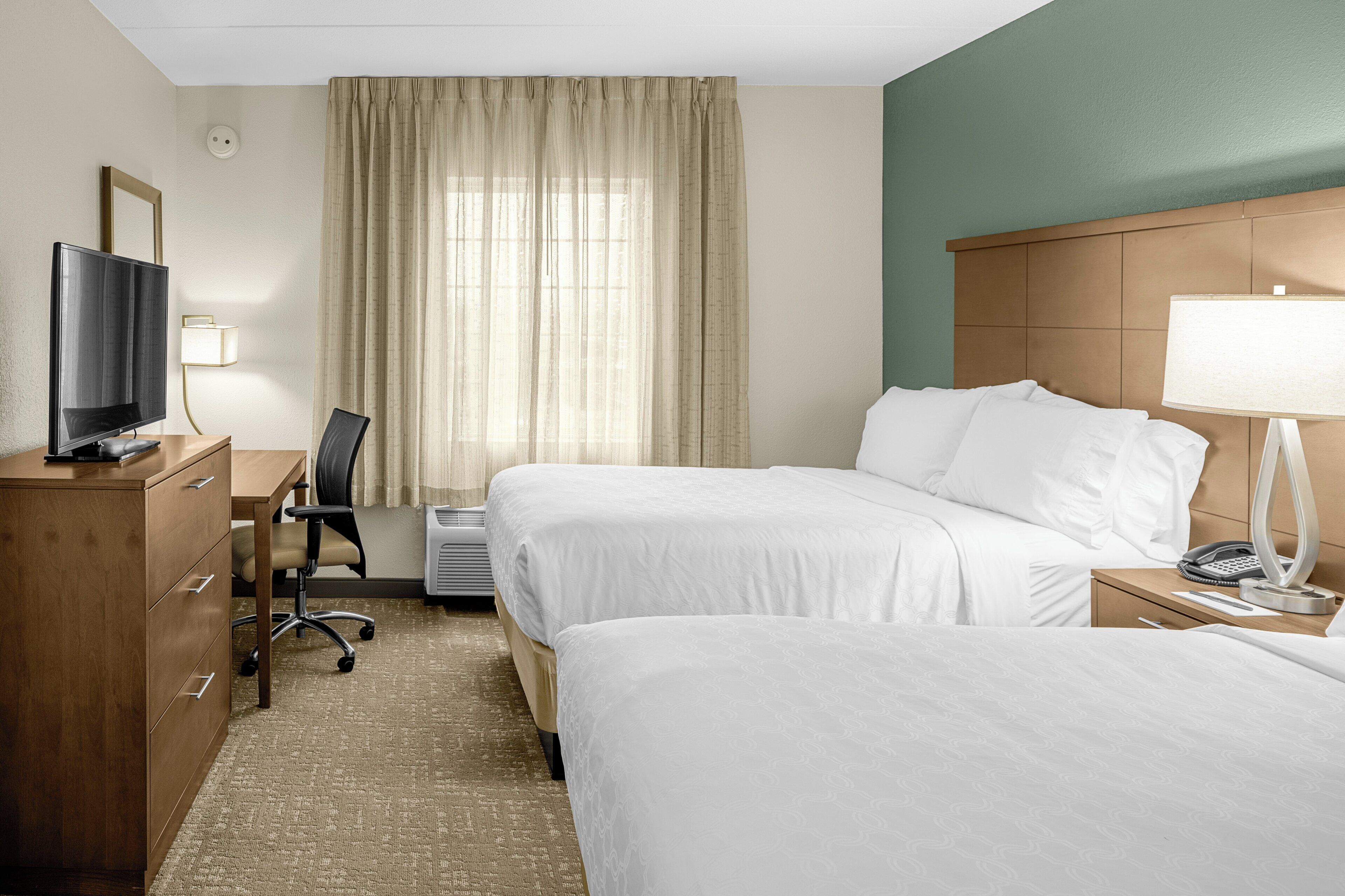 A hotel room with two beds, a desk with a chair, a television, a lamp, and a telephone.