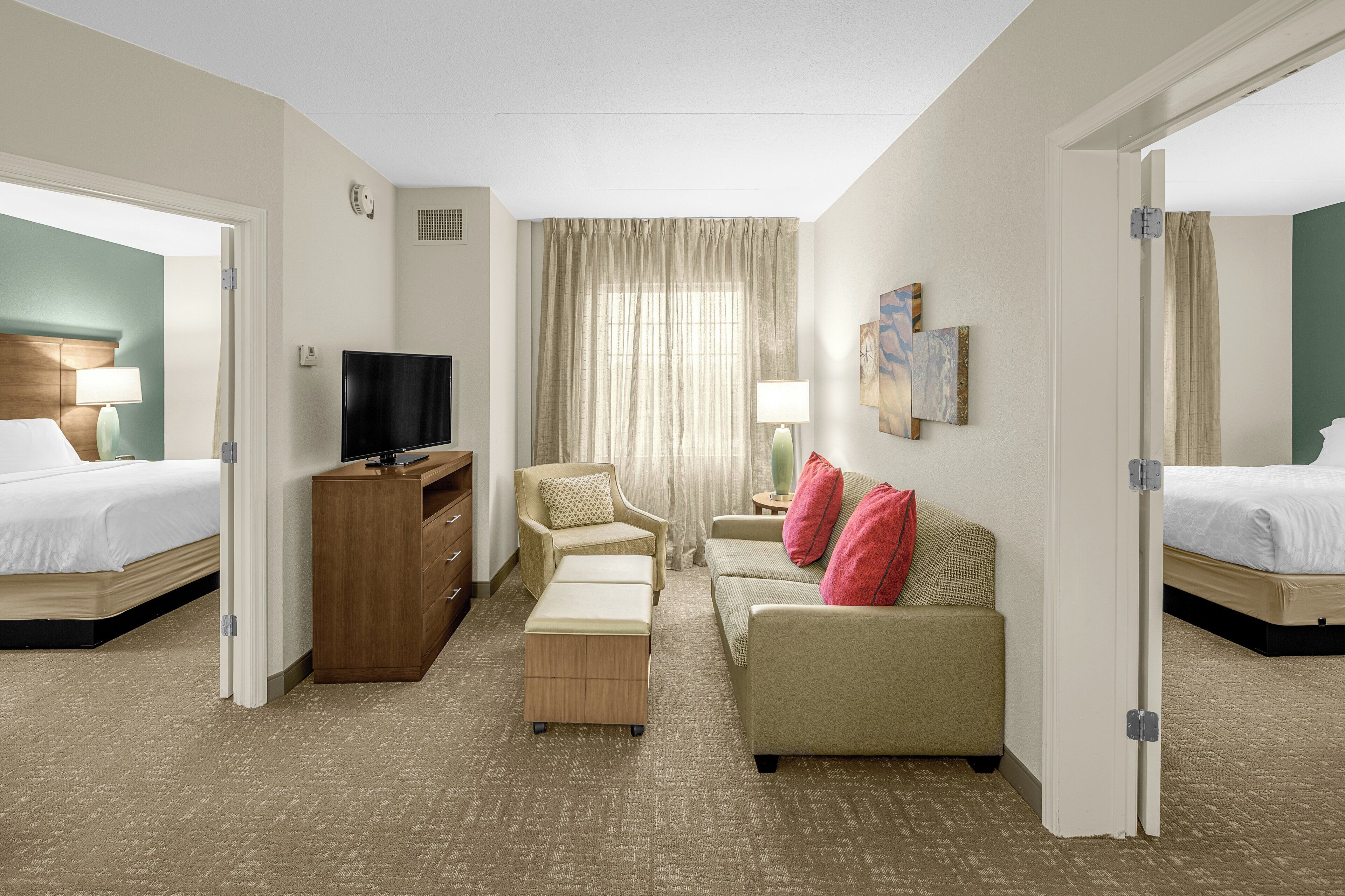 A hotel room with two beds, a TV, a sofa, and a small table.