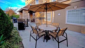 Une terrasse extérieure avec une table ronde et des chaises, un barbecue et un espace salon abrité.