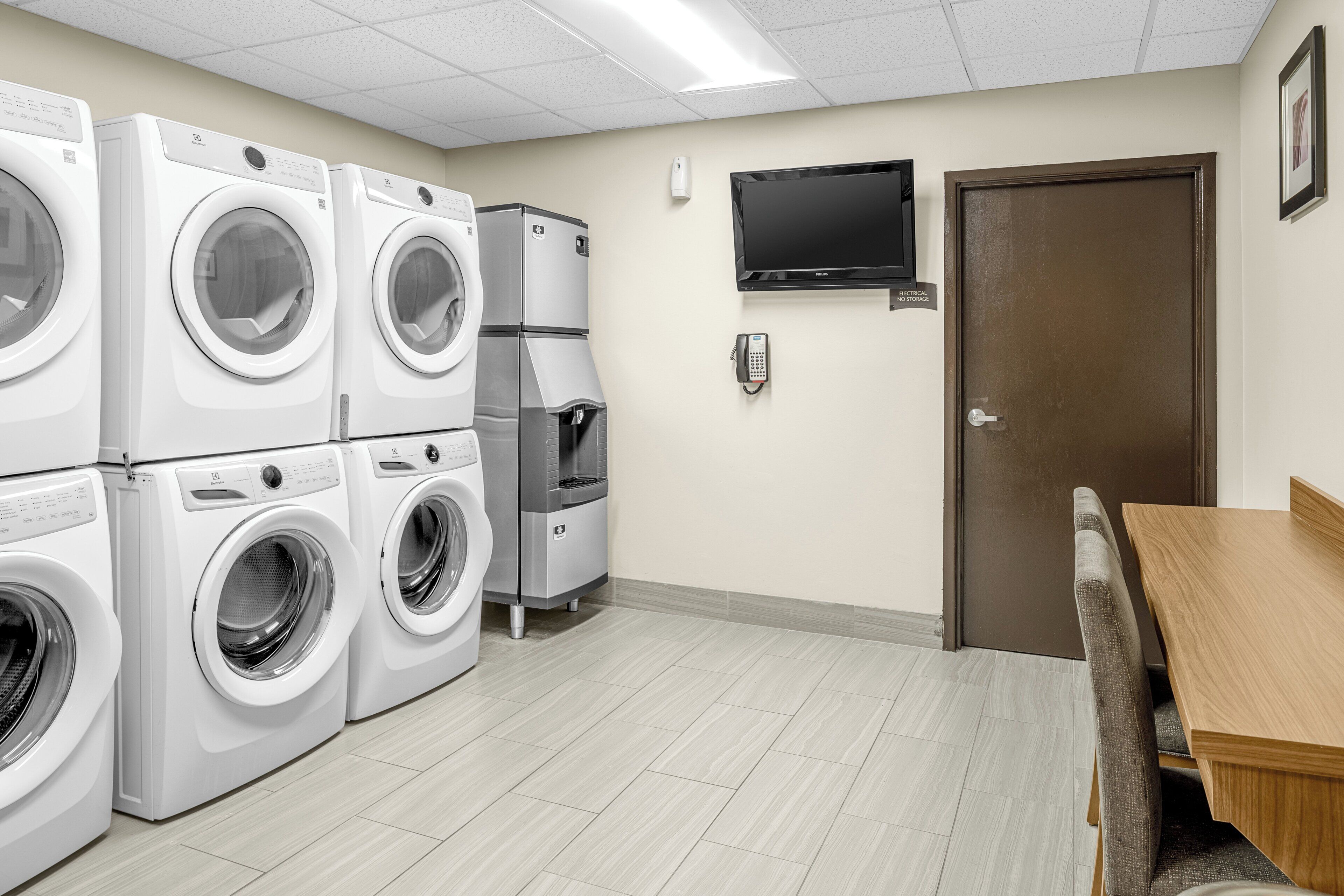 A laundry room with multiple washing machines, a refrigerator, a water cooler, a telephone, and a television mounted on the wall.