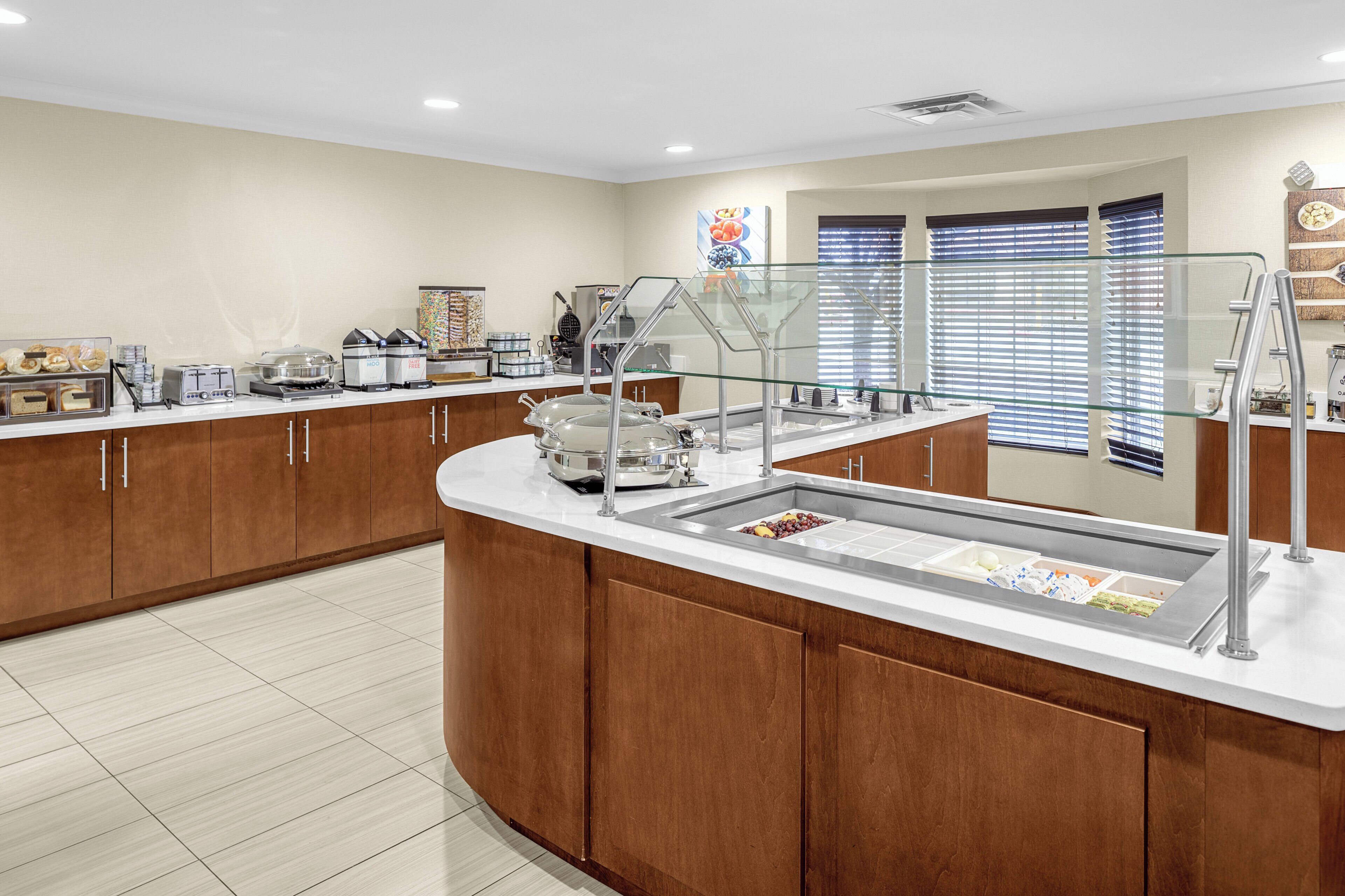 A buffet area with a variety of food items, a self-service station, and a window with blinds.