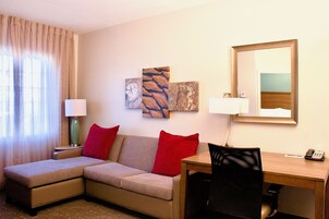 Habitación de hotel con sofá, escritorio, silla, dos lámparas y obras de arte en la pared.