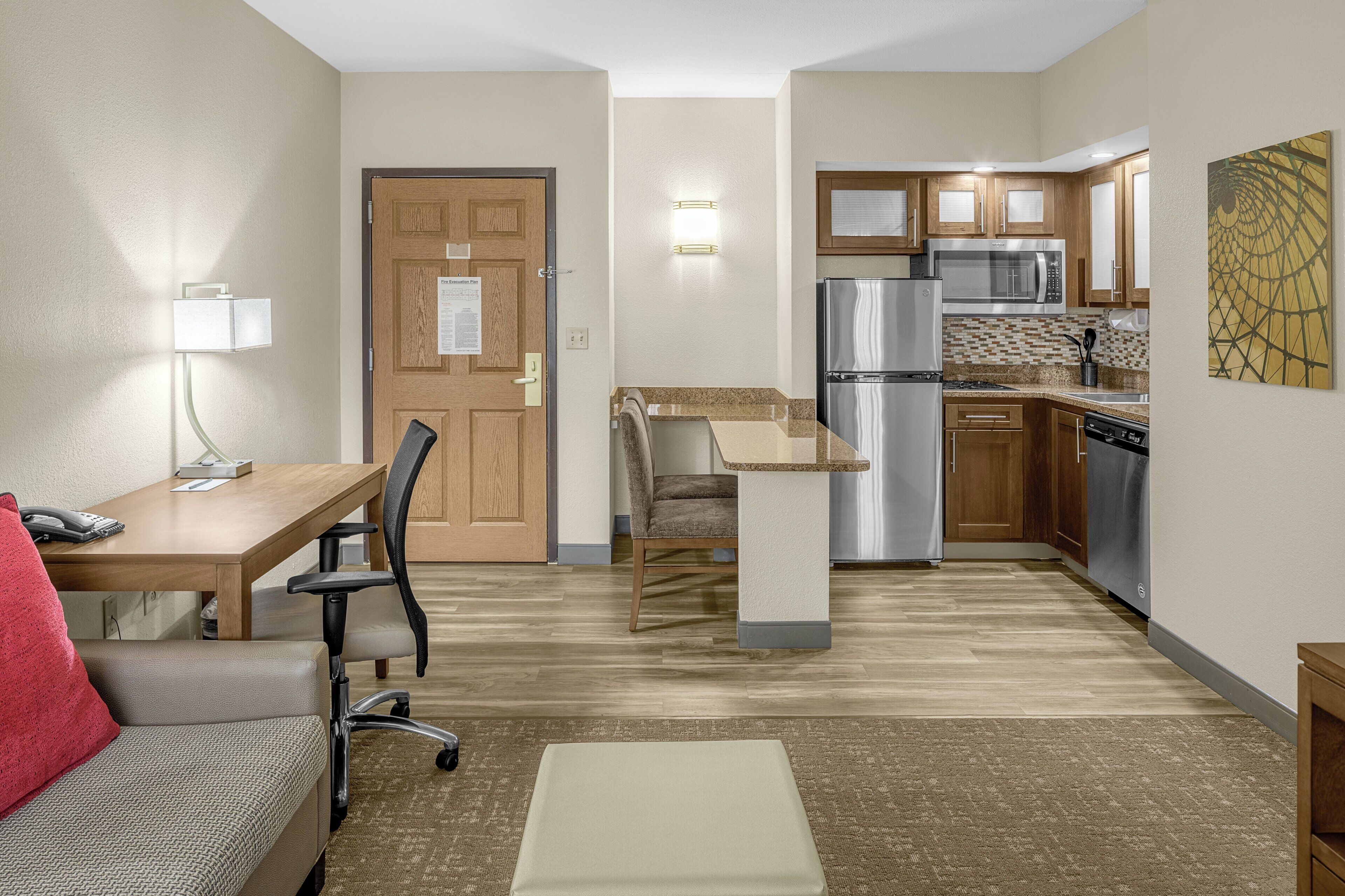 A compact hotel room with a kitchenette, a dining area with a table and chairs, and a small seating area with a sofa.